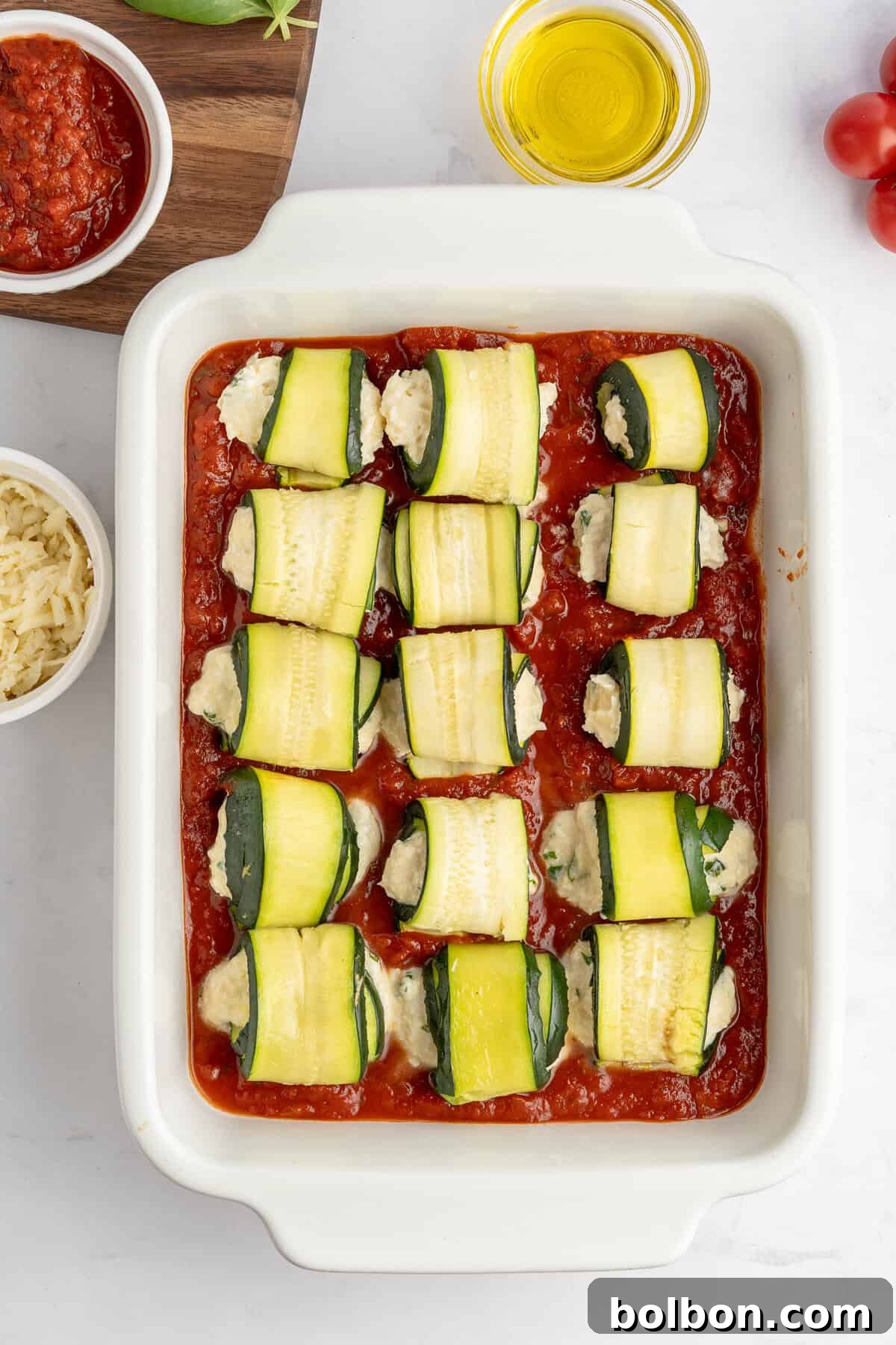 Marinara sauce in a baking dish with rolled up zucchini rolls in it 