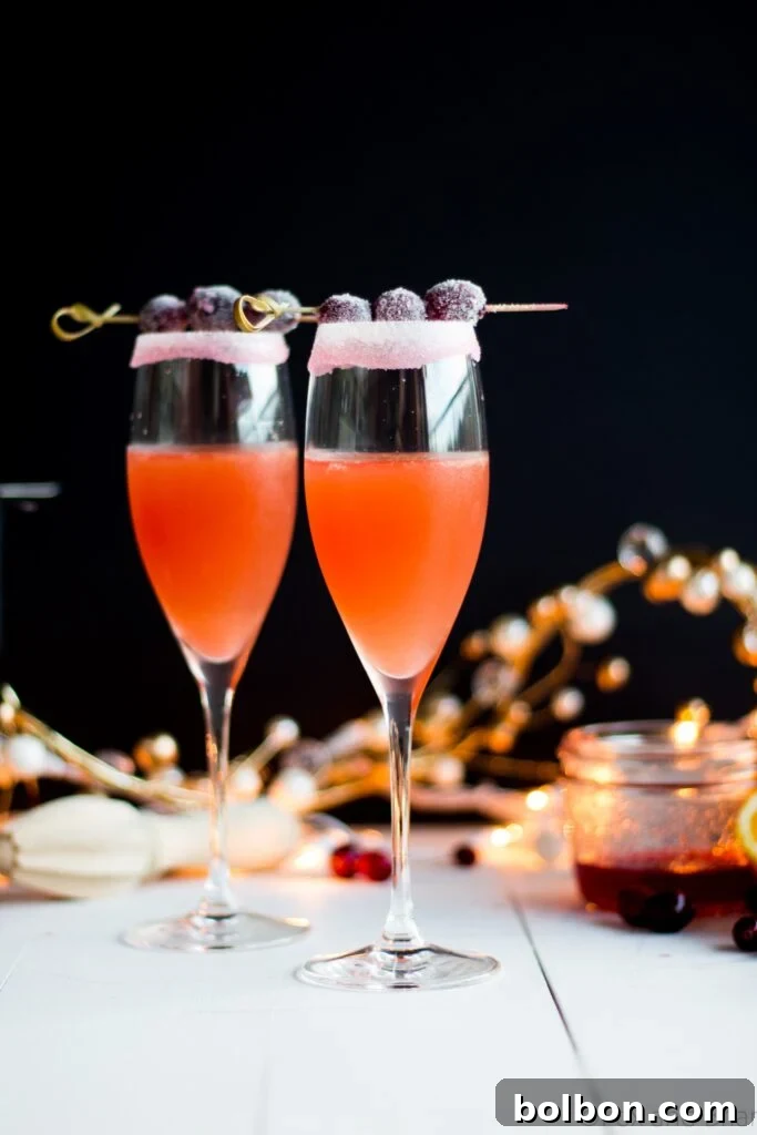 Two elegantly prepared Cranberry Orange Cosmos in martini glasses, featuring sugared rims and decorative cranberry skewers, ready for a festive toast.