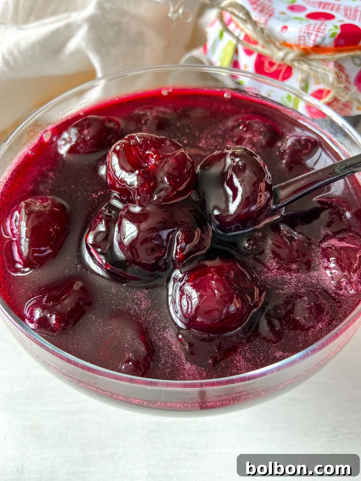 Handcrafted Cherry Preserve 2 Homemade Cherry Jam, glistening in a glass jar, showcasing whole cherries within its rich, red depths. Perfect for breakfast or dessert.