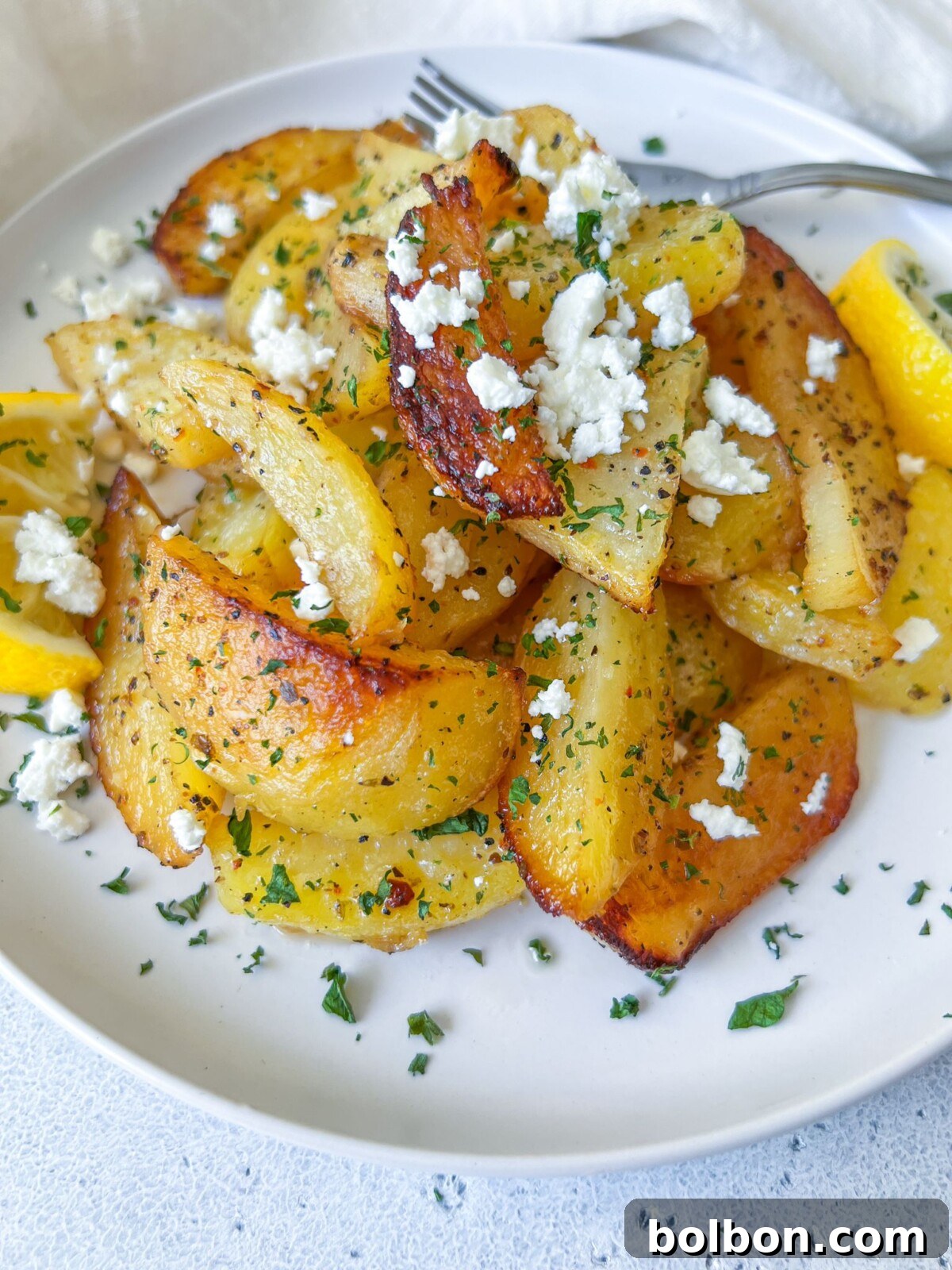 A rustic bowl filled with perfectly roasted Greek Potatoes, generously topped with crumbled feta cheese and fresh herbs, ready to be served.