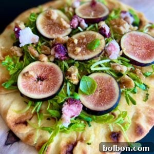 A flavorful Naan Pizza topped with fresh arugula, sliced figs, walnuts, goat cheese crumbles, and a drizzle of dressing served on a wooden board.