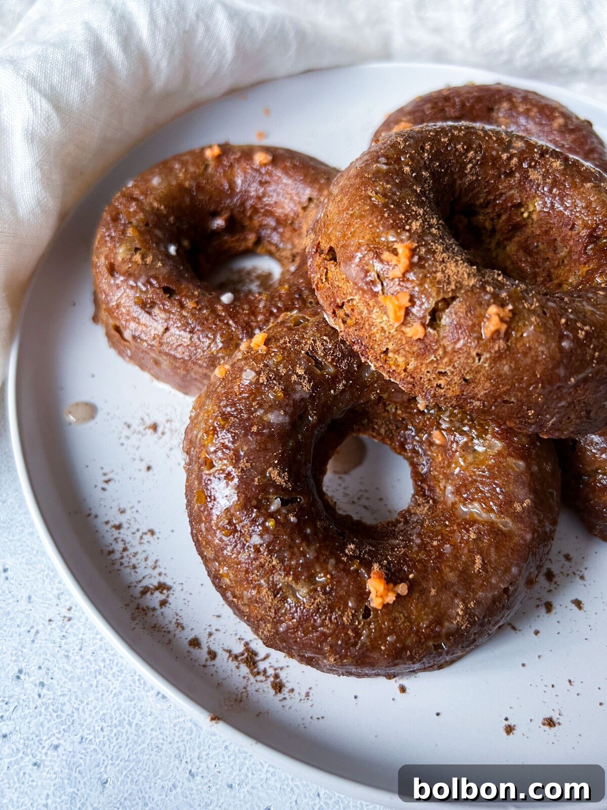 A white plate with freshly baked pumpkin spice donuts, beautifully glazed and adorned with a light dusting of spice, ready to be enjoyed as a delightful autumn treat.