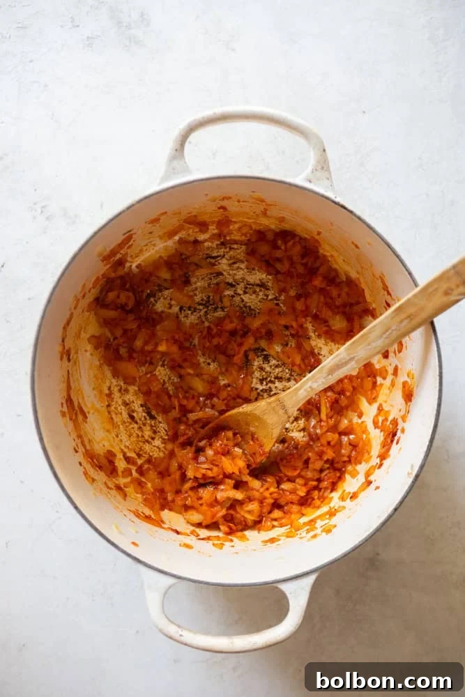 Diced onions and rich tomato paste being sautéed and stirred in a Dutch oven, creating a flavorful base for a hearty beef stew.