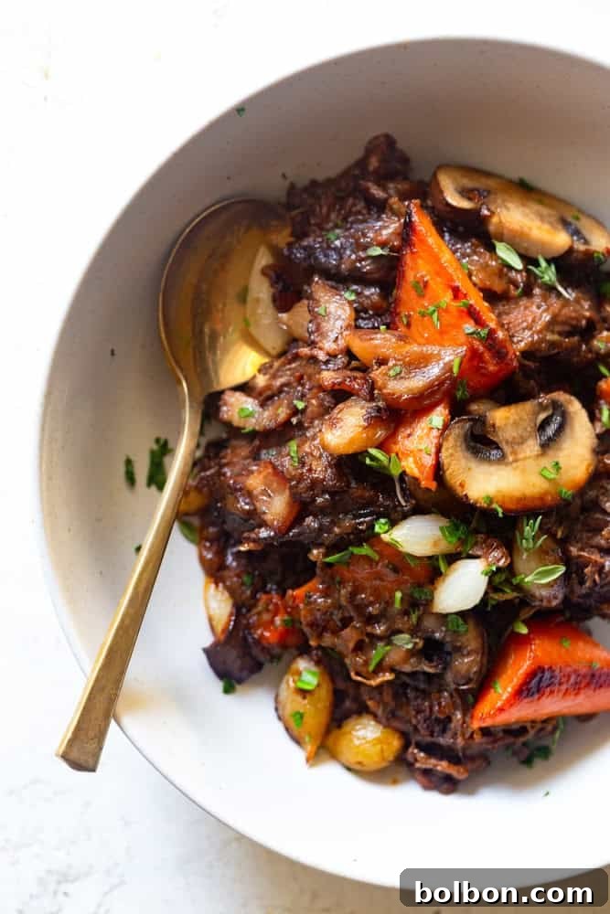 A close-up view of the delectable Red Wine Beef Stew served in a white bowl, featuring caramelized mushrooms, carrots, and pearl onions, highlighting its rich textures.