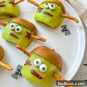 Spooky Franken-Kiwis 3 Sliced kiwis decorated as Frankenstein faces with candy eyes, chocolate-drawn mouths and scars, kiwi skin as hair, and pretzel sticks as bolts are a spooky treat—perfect alongside halloween mummy hotdogs for your festive celebration.