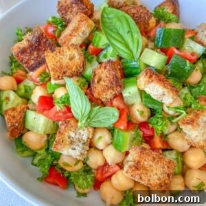 A bowl of Chickpea Crouton Salad with diced cucumbers, tomatoes, fresh parsley, crunchy croutons, and basil leaves.