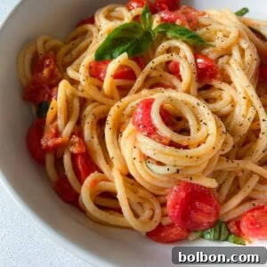 A bowl of Cherry Tomato Pasta with fresh basil and a sprinkle of black pepper, served in a white dish on a light surface.