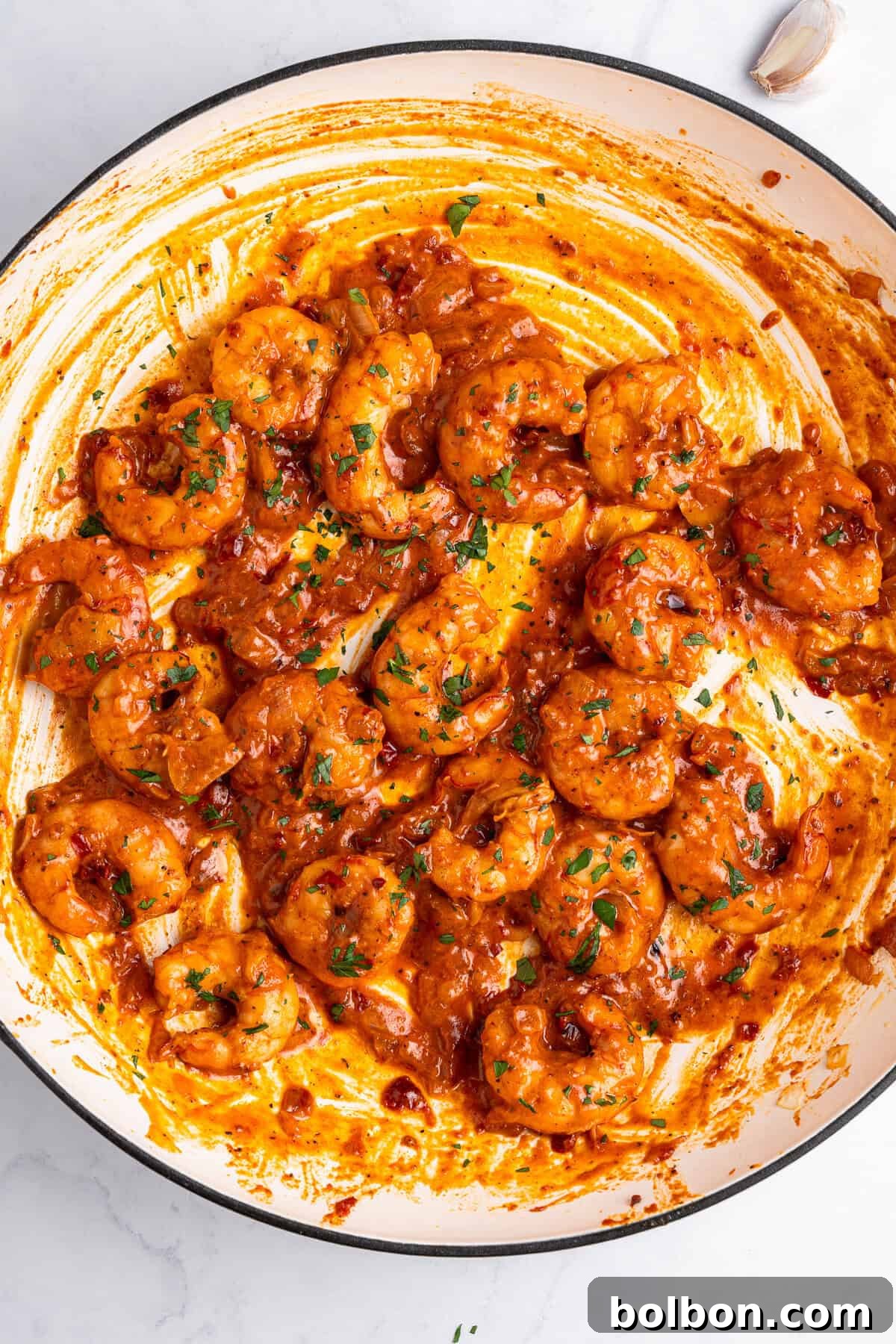 A skillet filled with cooked Creamy Tuscan shrimp in a rich, tomato-based sauce garnished with chopped herbs. The sauce has an orange-red hue, coating the shrimp thoroughly. The dish appears flavorful and spicy.