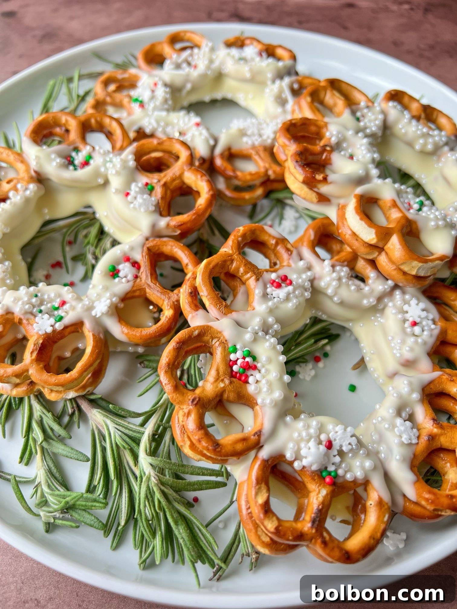 Close-up of a Pretzel Christmas Wreath with white chocolate and red, green, and white sprinkles, resting on parchment paper.