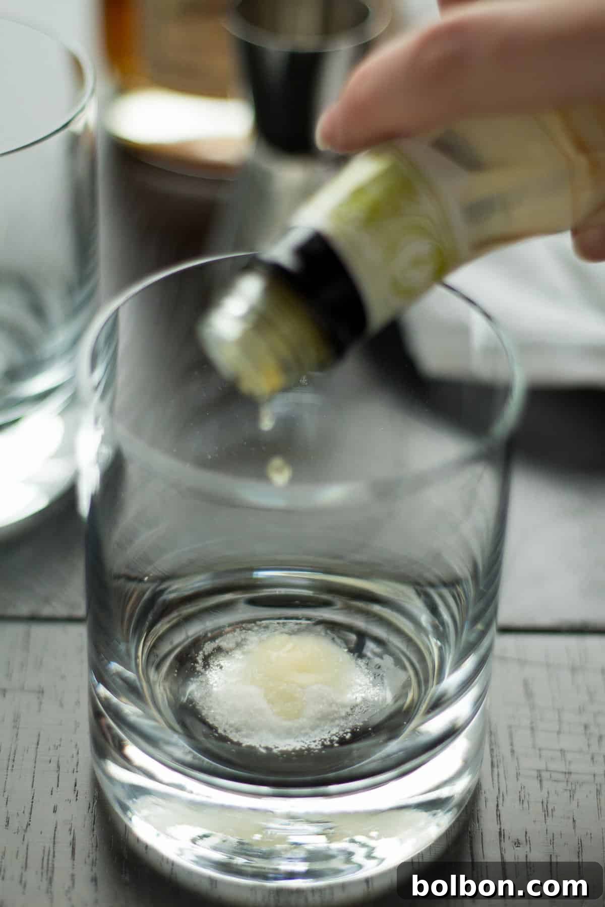 The process of muddling orange zest, sugar, and bitters in a lowball glass, preparing the base for an Apple Old Fashioned.