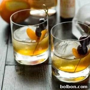 A vibrant Apple Old Fashioned cocktail garnished with an orange slice and cherry.
