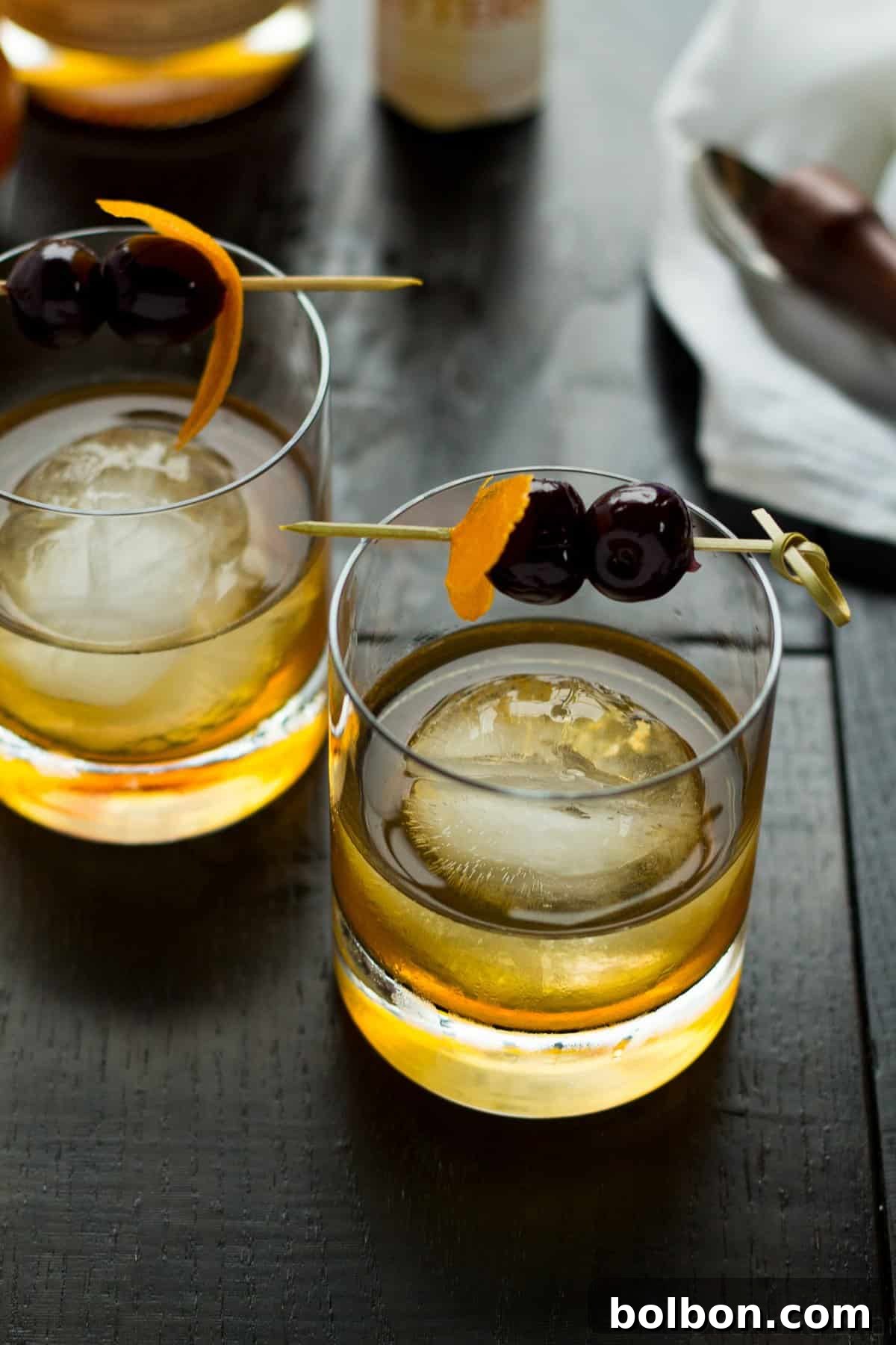 The Apple Old Fashioned, beautifully presented with an orange peel and cherries, ready for a delightful sip.