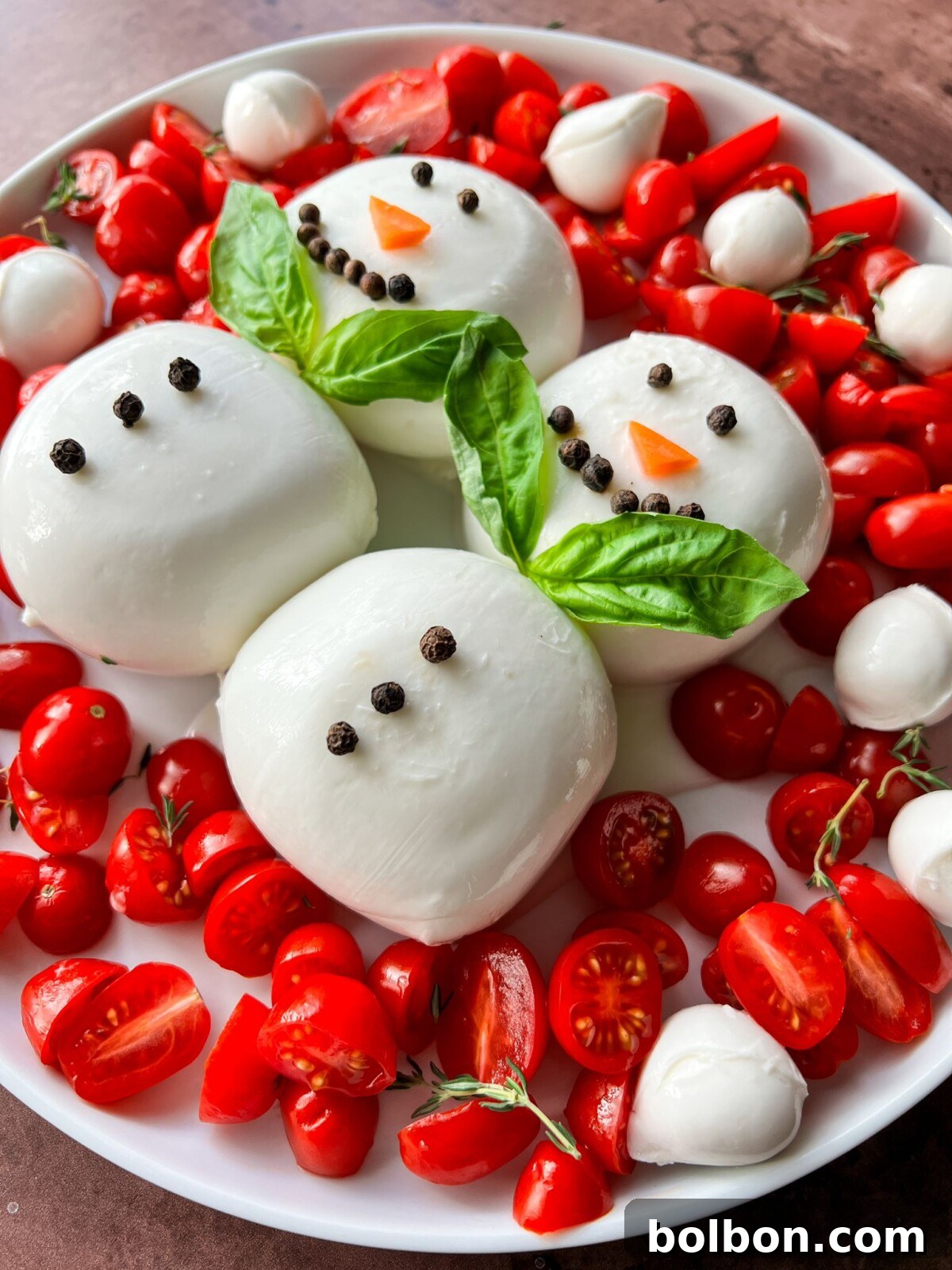 Frosty Burrata Fantasy 2 Two adorable Burrata Snowmen on a platter, surrounded by halved cherry tomatoes, bocconcini, and basil leaves, beautifully drizzled with balsamic glaze, set against a festive backdrop.