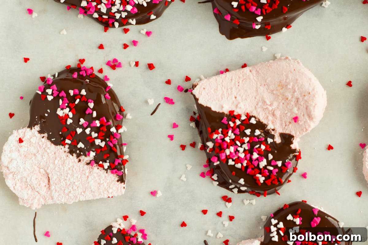 Pillowy soft homemade strawberry marshmallows in heart shapes, some dipped in chocolate and adorned with sprinkles, perfect for Valentine's Day.
