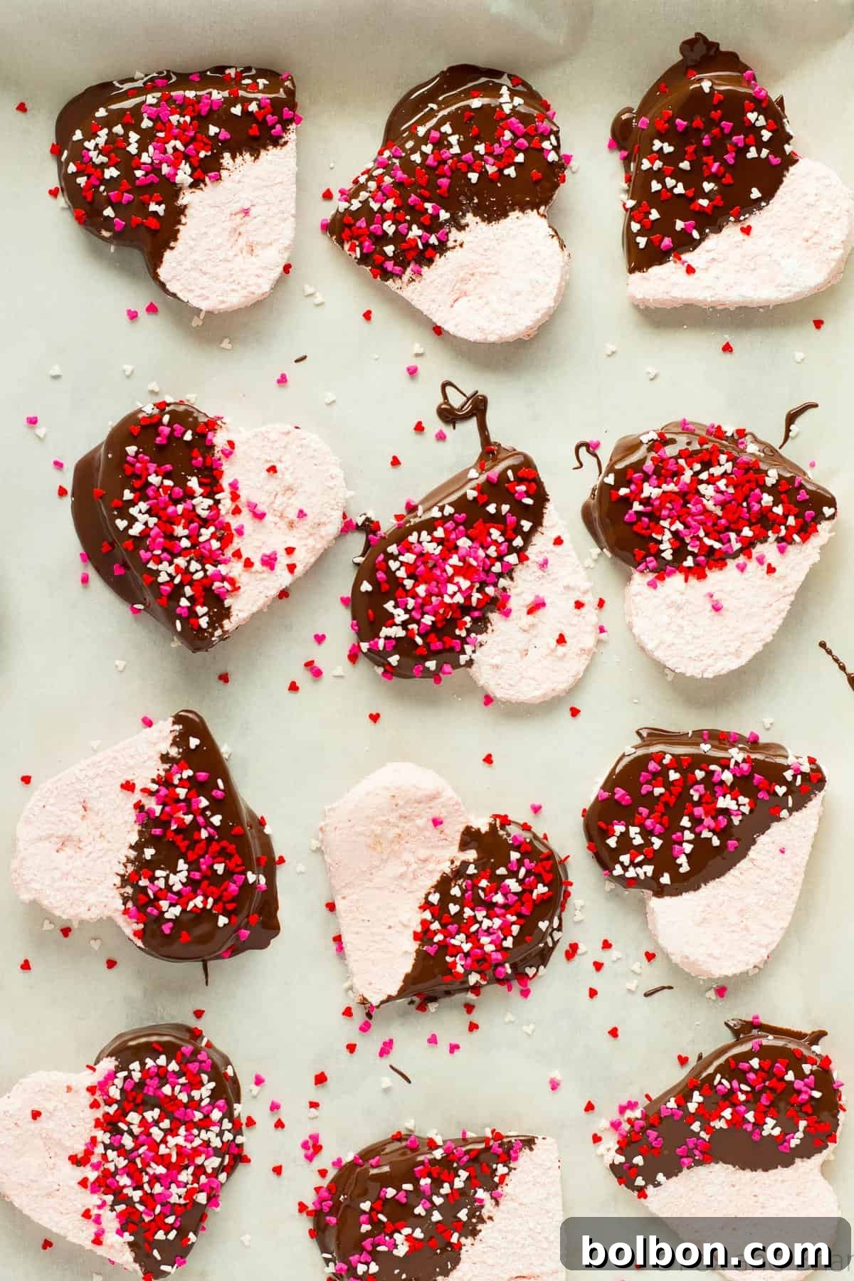 An array of homemade strawberry marshmallows, some shaped as hearts and dipped in chocolate with sprinkles, displayed beautifully on a plate.