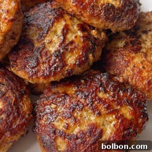 A close-up of several golden-brown, pan-fried sausage patties stacked on a white plate. The crispy, caramelized exterior and juicy texture make them perfect for anyone looking for an Easy Meatball Recipe alternative.