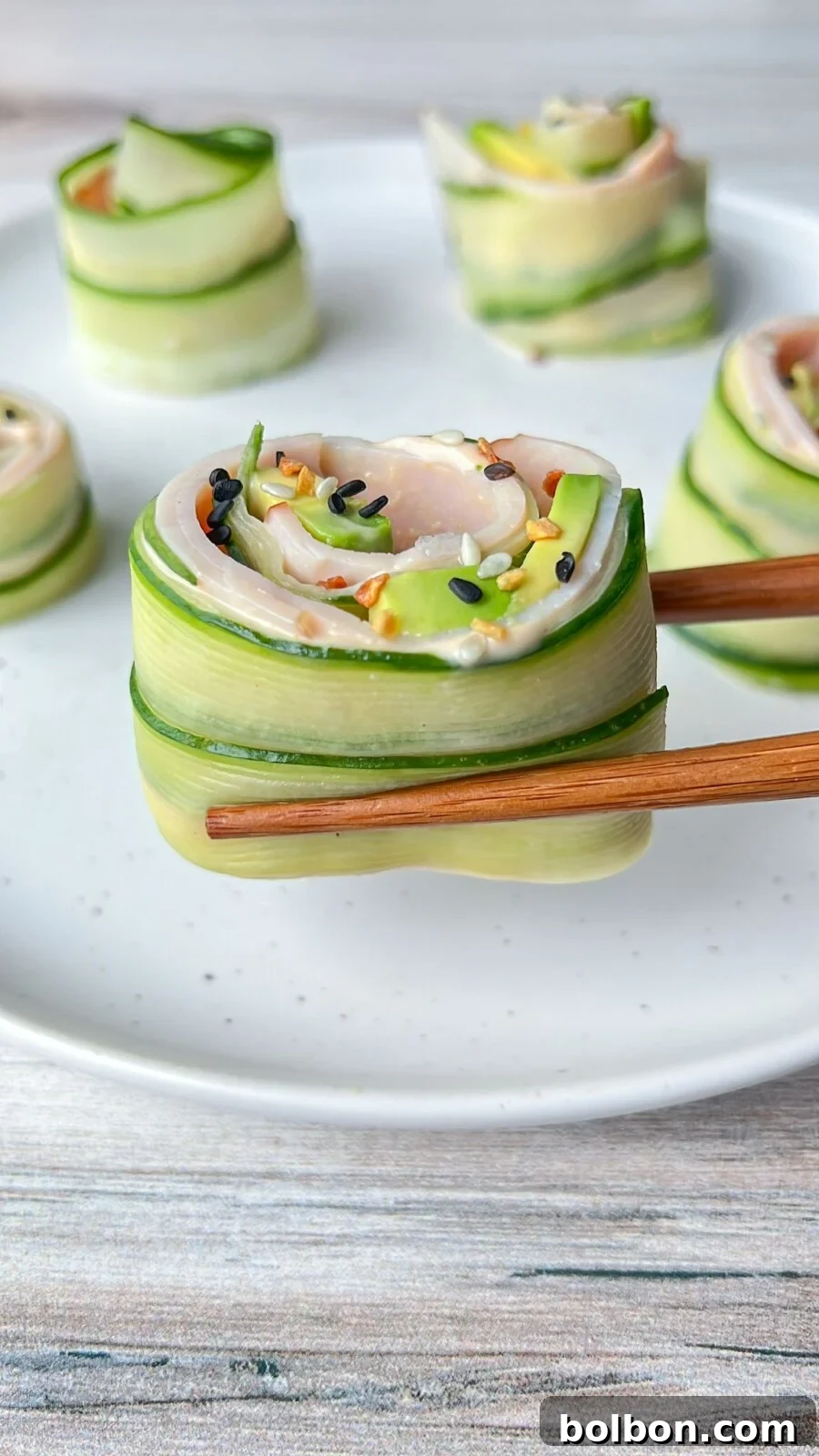 Freshly prepared Cucumber and Avocado Rolls, garnished with sesame seeds and herbs, are arranged on a white plate, ready to be served as a healthy, low-carb snack or appetizer.