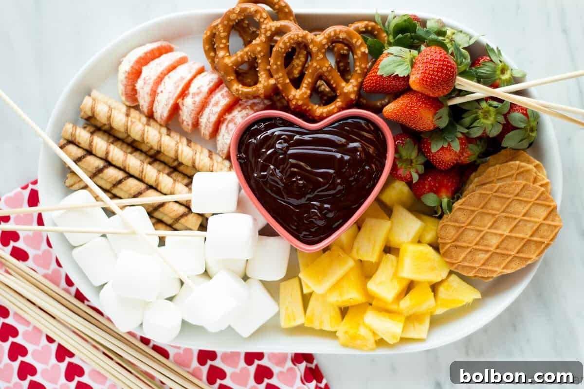 An inviting spread of dark chocolate fondue with a variety of dippers including strawberries, pineapple, marshmallows, and pretzels, ready for a fun dessert.