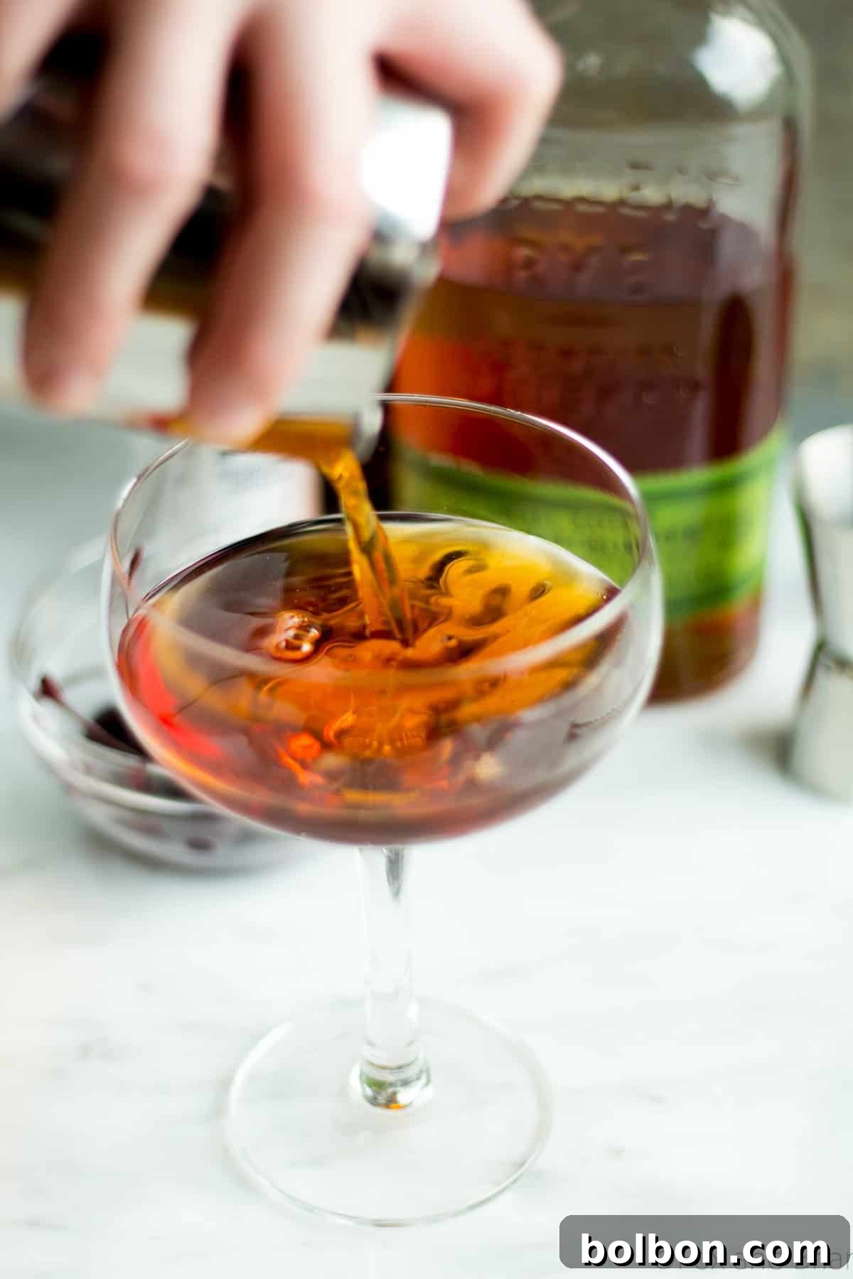 Crafting the Timeless Manhattan 4 A hand stirring a Manhattan cocktail in a chilled mixing glass filled with ice, preparing it for straining and serving.