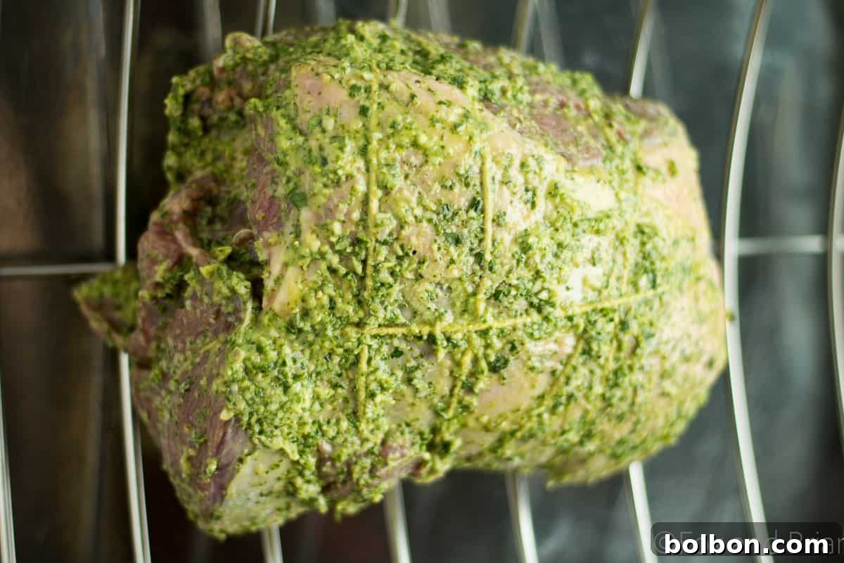 Boneless leg of lamb being coated with fresh herb paste before rolling.