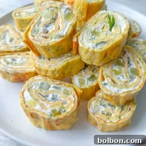 A plate of Zucchini Egg Roll pinwheels filled with cream cheese and diced vegetables, garnished with a sprig of fresh dill, displayed on a white plate.