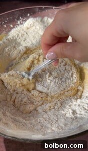 A hand holding a fork mixes flour with a wet dough mixture in a bowl, starting the process of combining ingredients for baking delicious Apple Cookies (Scones).