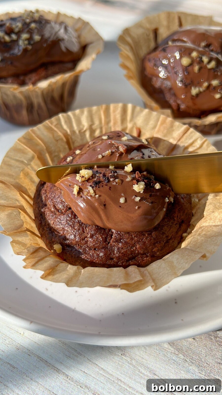 Healthy Chocolate Muffins - Two freshly baked chocolate muffins, one with a bite taken out, resting on a white plate, highlighting their appealing interior.