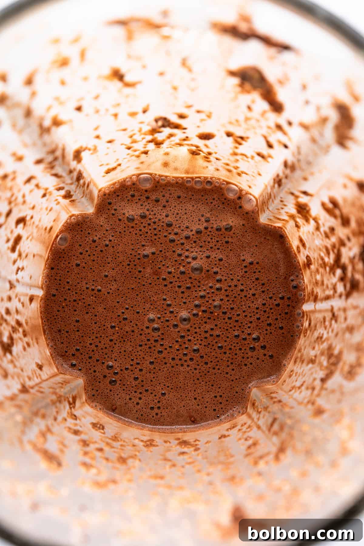 Fudgy Chocolate Oat Bar 5 A close-up view of a blender container with chocolate smoothie remnants clinging to the sides. The bottom shows a frothy, rich chocolate mixture with small bubbles.