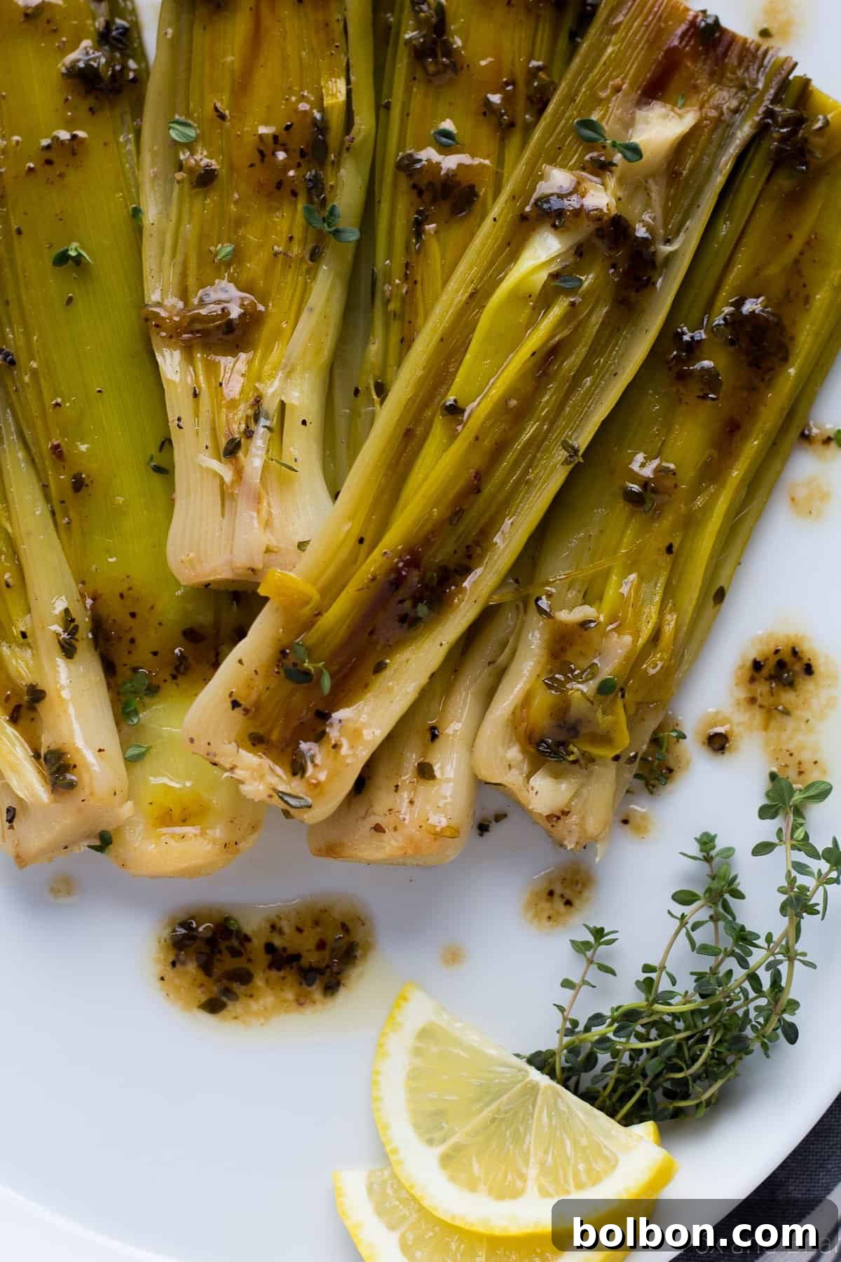 Velvety Braised Leeks 7 A plate of perfectly braised leeks, artfully arranged and drizzled with a rich butter, wine, and lemon sauce, garnished with fresh herbs.