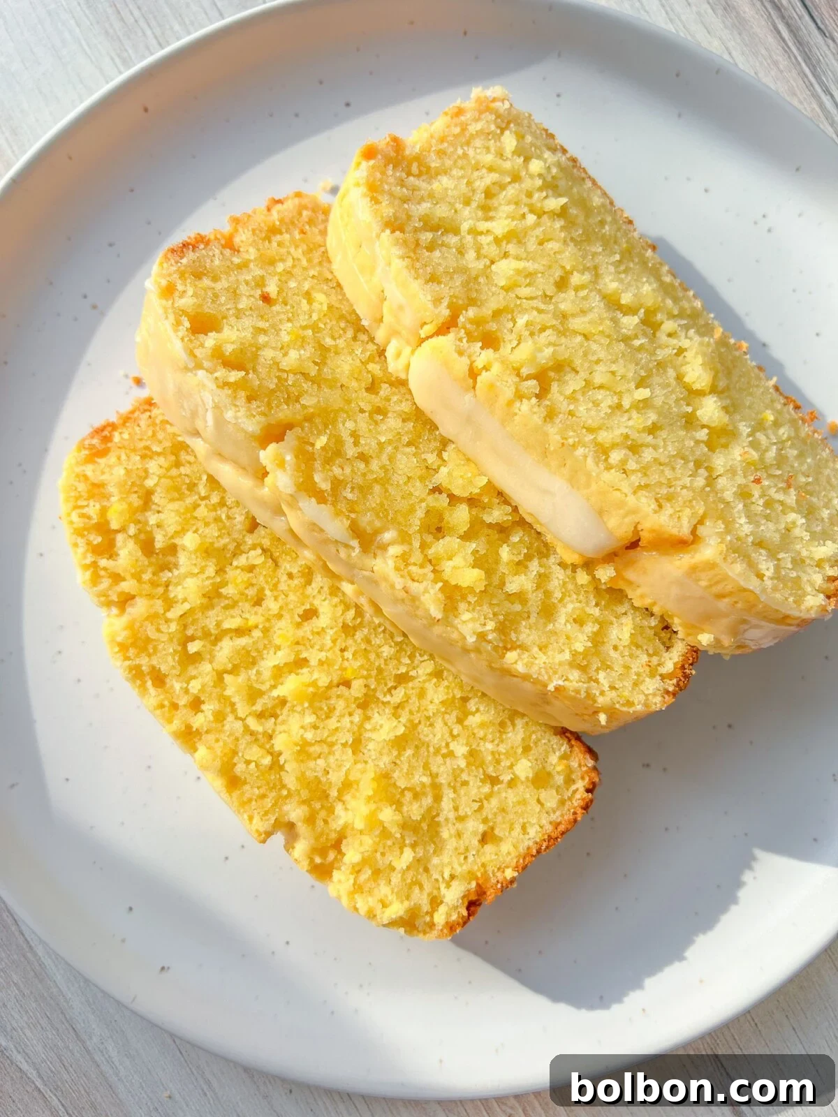 Zesty Whole Lemon Blender Cake 3 A close-up of a perfectly baked Whole Lemon Blender Cake, still in its loaf pan, on a marble countertop with two whole Meyer lemons next to it. The golden-brown crust promises deliciousness.
