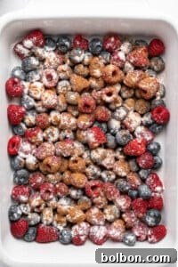 Summer Berry Crunch 7 A white baking dish filled with fresh raspberries and blueberries, sprinkled with powdered sugar and cinnamon.