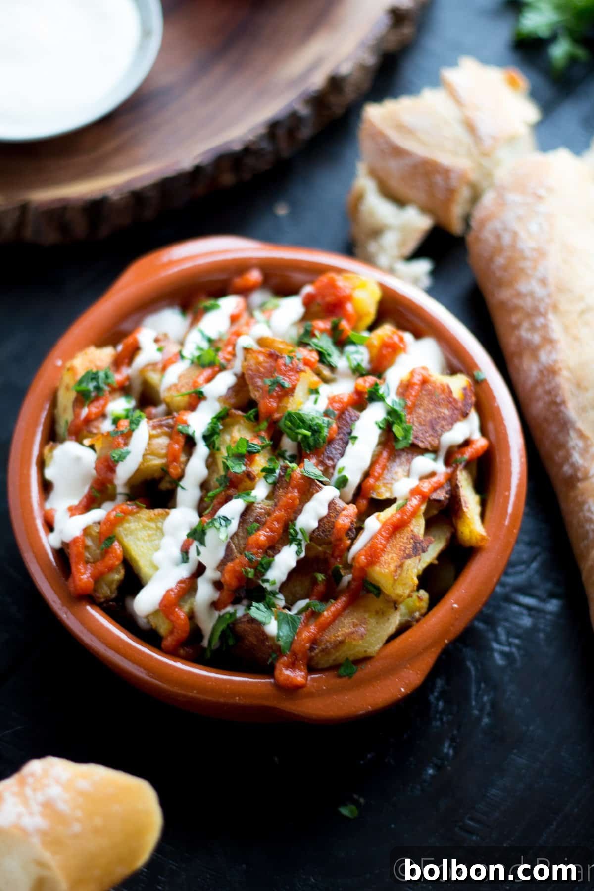 Ultimate Patatas Bravas Guide 6 Close-up of a rustic bowl filled with crispy Patatas Bravas, adorned with bright red salsa brava.