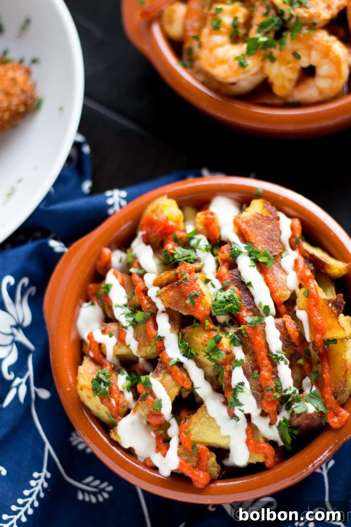 Ultimate Patatas Bravas Guide 8 A vibrant bowl of Patatas Bravas, perfectly dressed with red salsa brava and white aioli, garnished with green parsley.