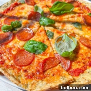 A close-up of a Low Carb Pizza topped with pepperoni and fresh basil leaves, sliced into pieces and served on a white plate. The melted cheese and tomato sauce are visible in bright, natural sunlight.
