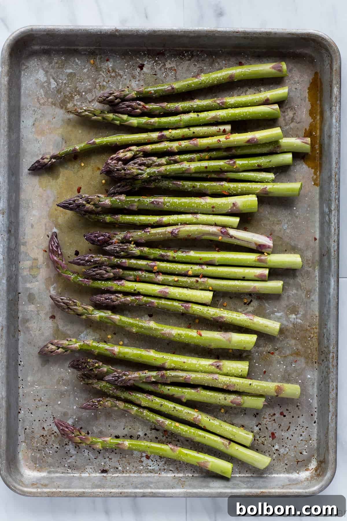 Close-up shot of seasoned raw shrimp and fresh asparagus spears arranged on a baking sheet, ready for roasting.