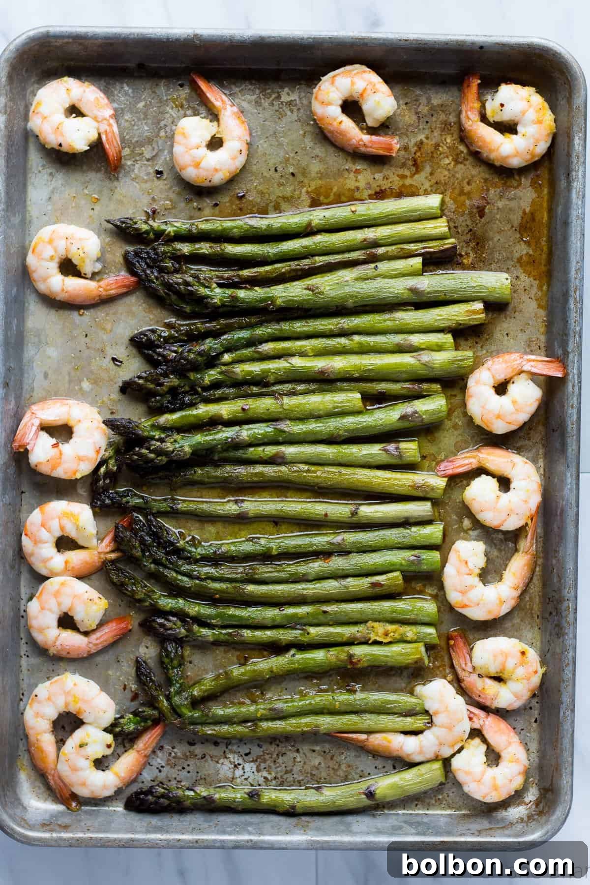 Colorful close-up of perfectly roasted shrimp and bright green asparagus on a baking sheet, glistening with olive oil.