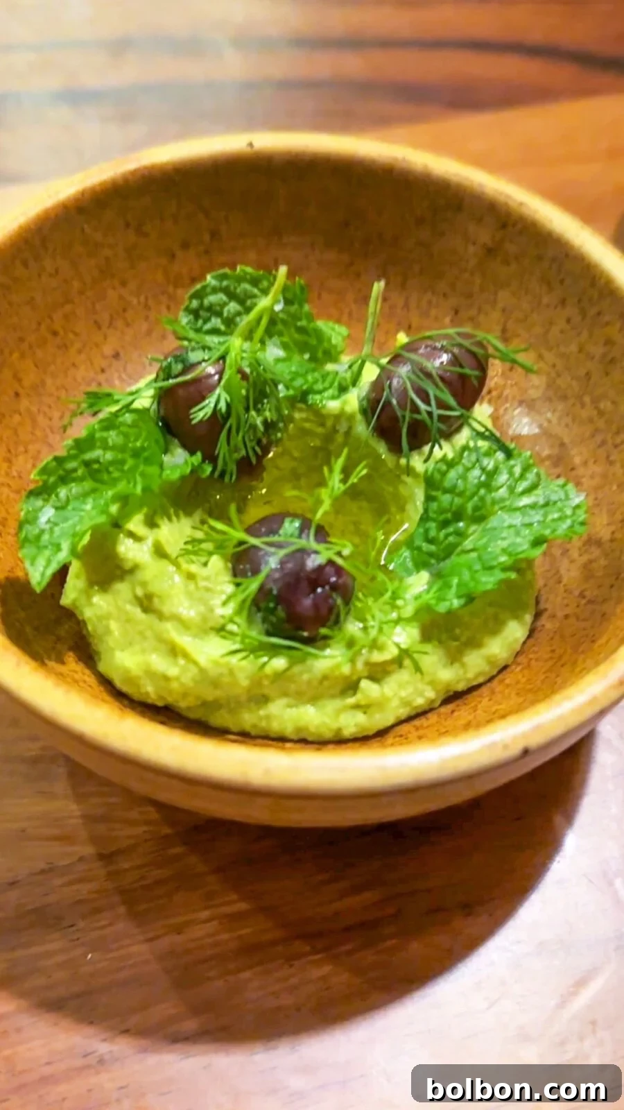 Freshly made Avocado Hummus in a bowl, garnished with herbs and a drizzle of olive oil, accompanied by homemade Tajin tortilla chips.