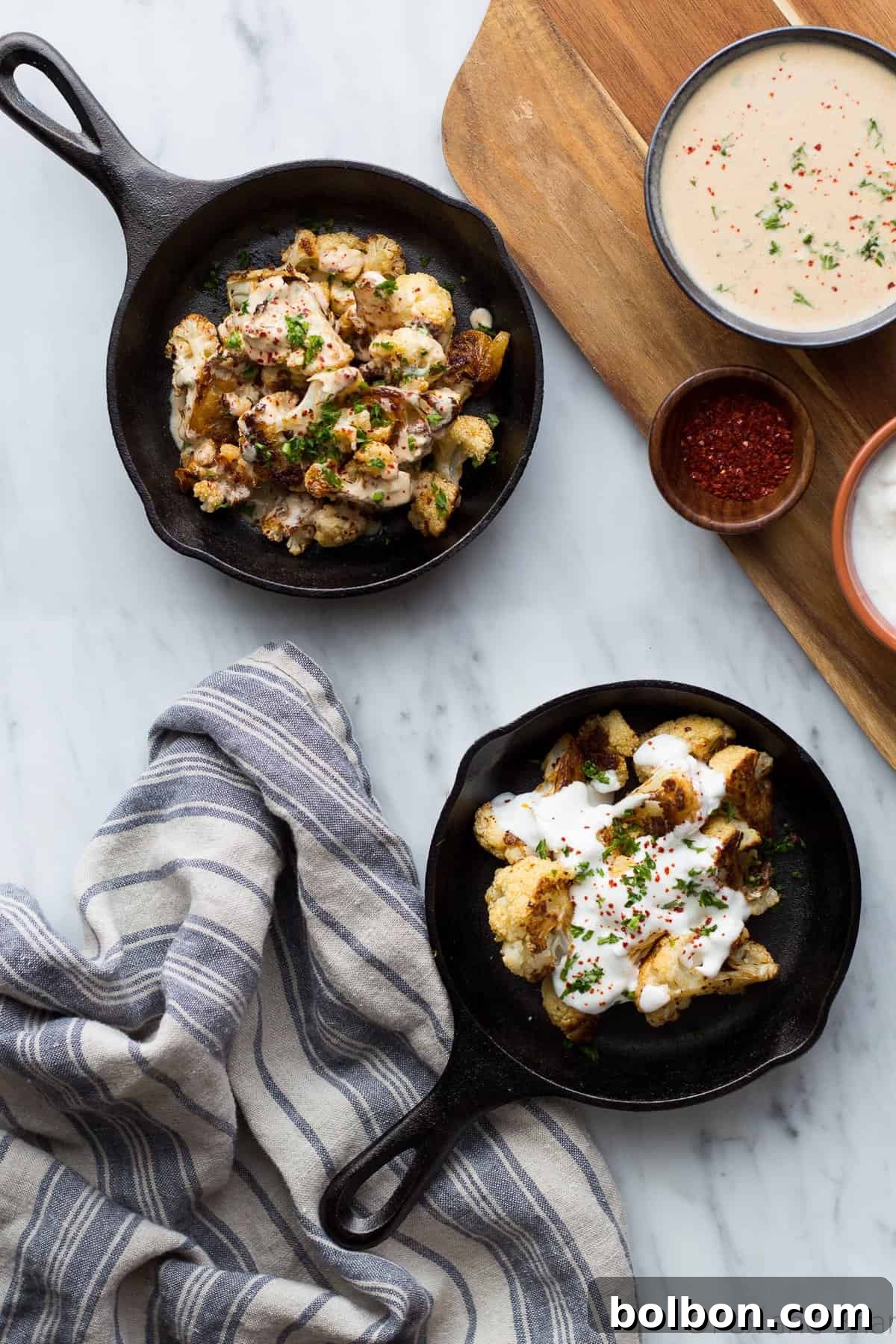 A top-down view of roasted cauliflower, garnished with fresh herbs and a drizzle of rich tahini sauce.