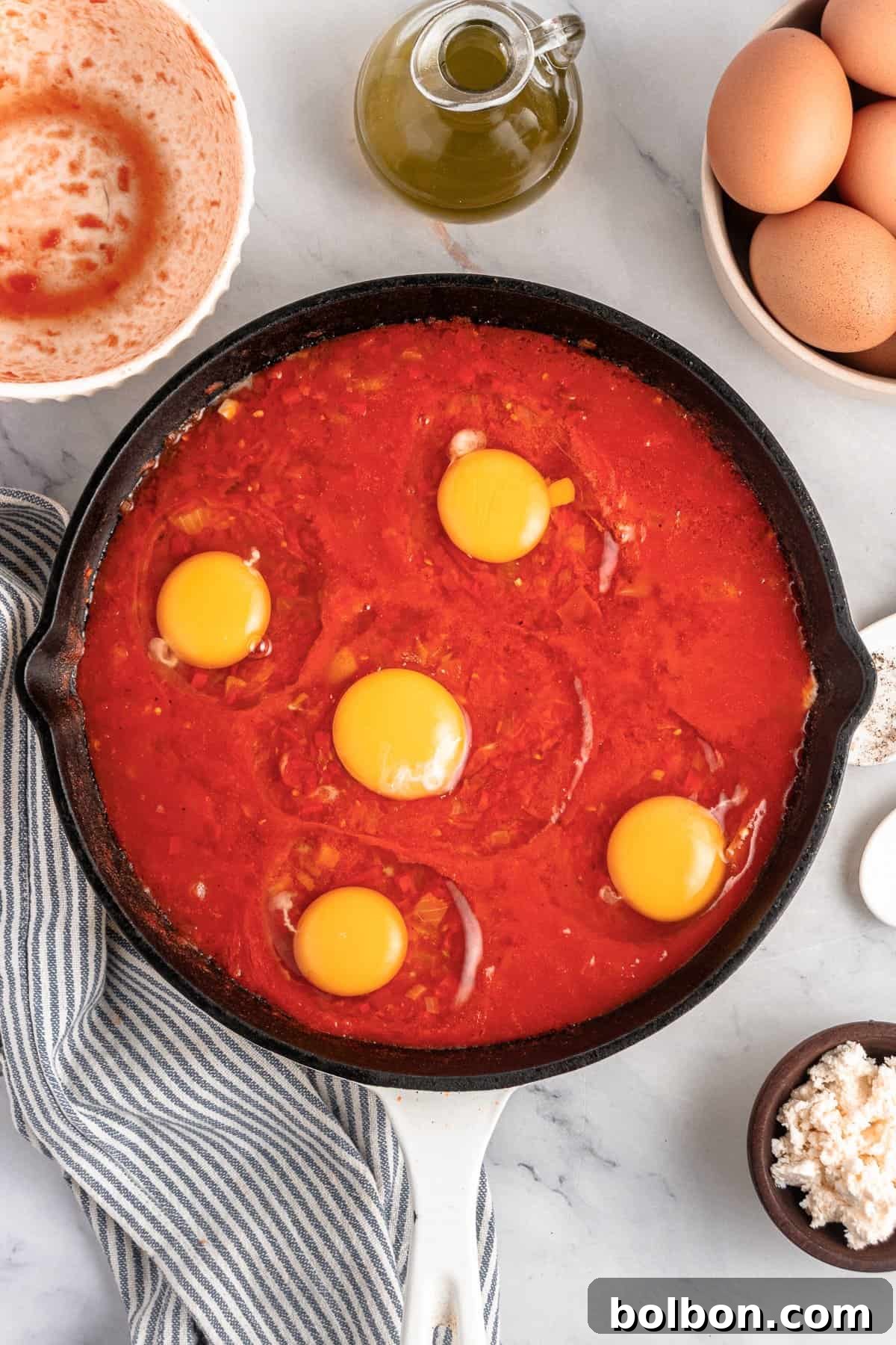 A skillet with cracked eggs on top of the tomato sauce. 