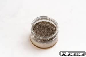 A small glass jar filled with chia seeds, partially submerged in a liquid, sits on a white surface.