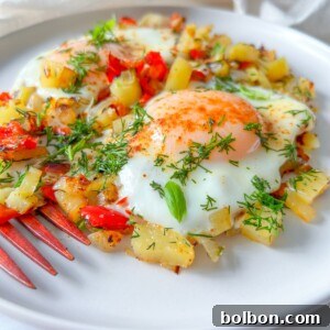 A close-up of two fried eggs served on a bed of sautéed diced potatoes and red bell peppers, garnished with fresh herbs on a white plate with a red fork.
