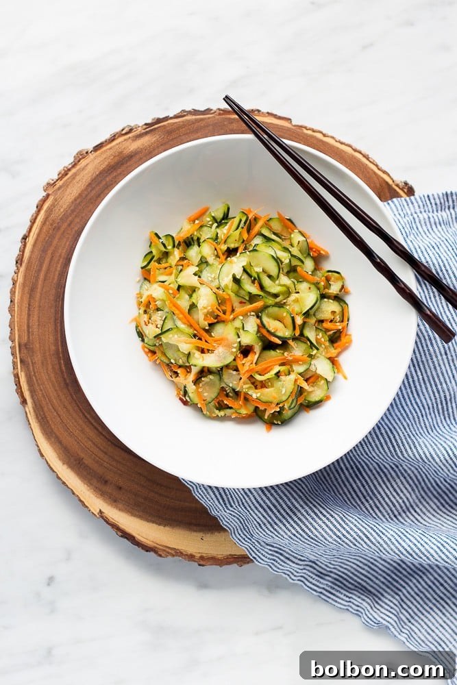 Hand tossing a medley of spiralized cucumbers and grated carrots with a savory sesame dressing.