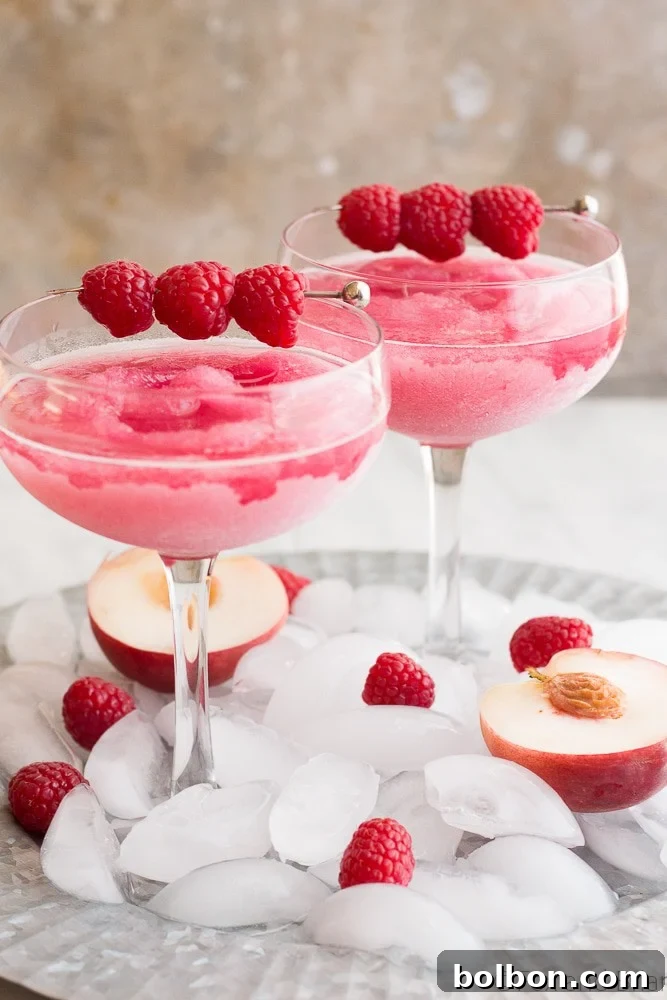Close-up of a glass of Raspberry Peach Frosé with raspberries and a peach slice.