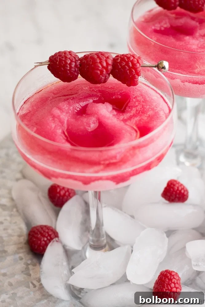 A glass of Raspberry Peach Frosé garnished with fresh raspberries and a peach slice.