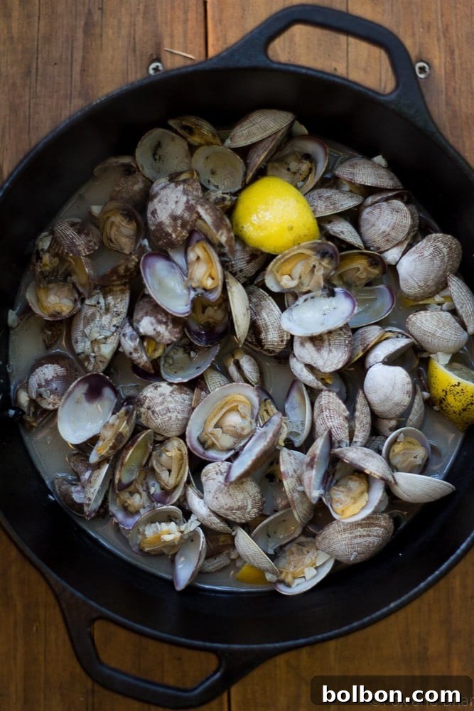 Ingredients for Beer Steamed Clams including fresh Manila clams, lemon, garlic, butter, and a can of beer, prepared for cooking.
