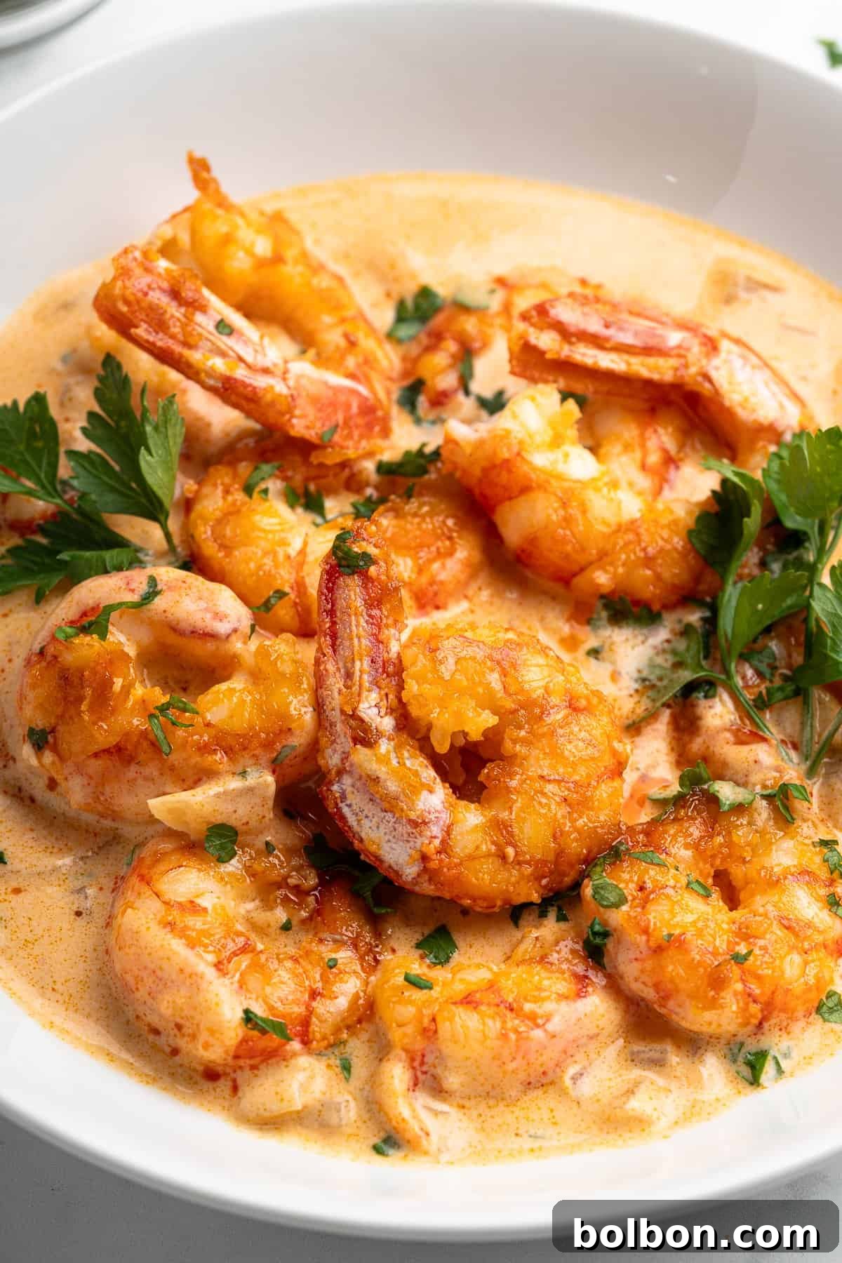 A pristine white bowl filled with a creamy, inviting orange sauce and plump, cooked shrimp, elegantly garnished with vibrant fresh parsley. The golden shrimp are luxuriantly immersed in the rich sauce, creating a flavorful and visually enticing dish.