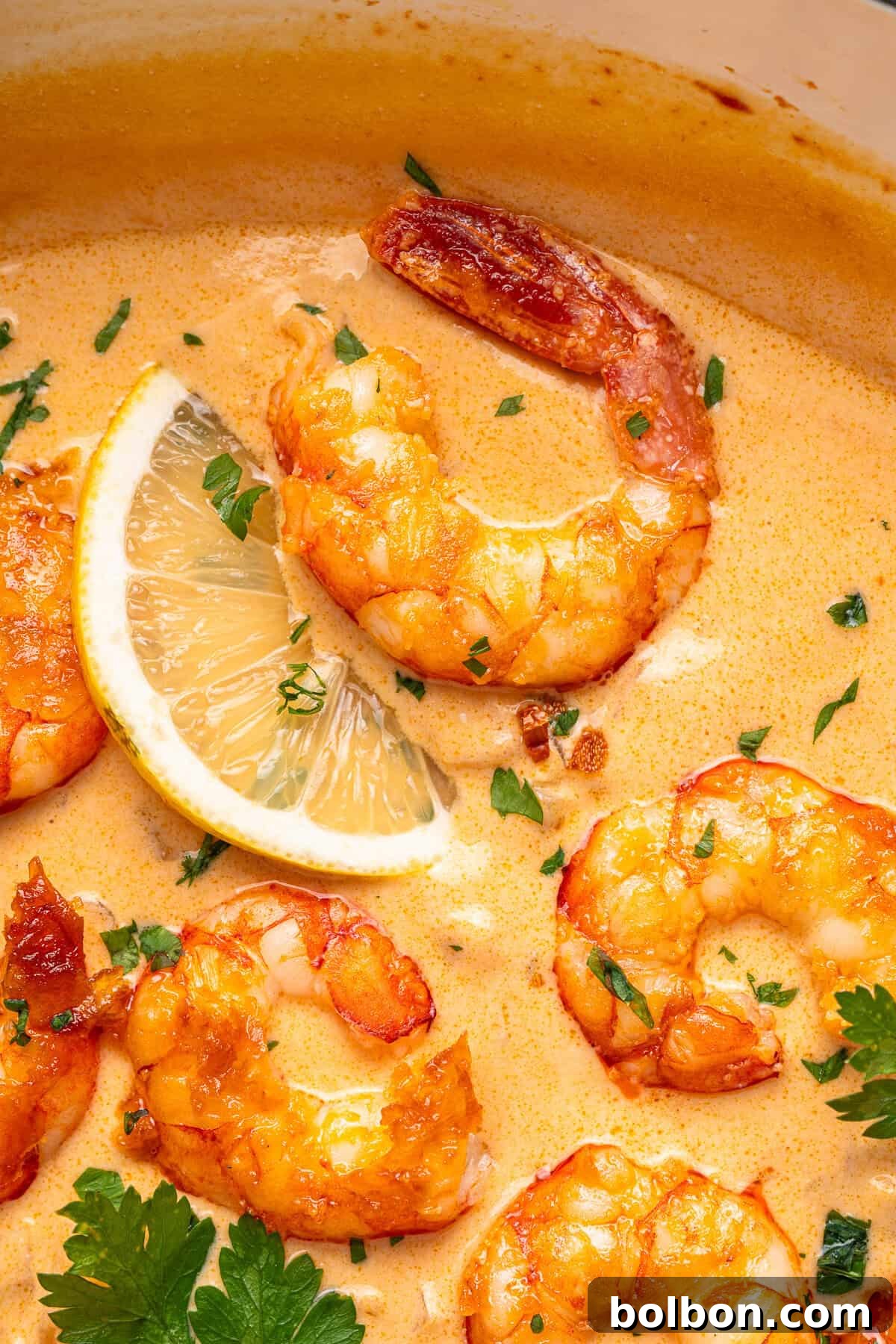 A visually stunning creamy shrimp dish, artfully garnished with fresh herbs and a vibrant lemon wedge. The shrimp are perfectly cooked and enveloped in a rich, warm orangish sauce, with finely chopped herbs sprinkled generously on top, creating an appetizing and lively presentation.