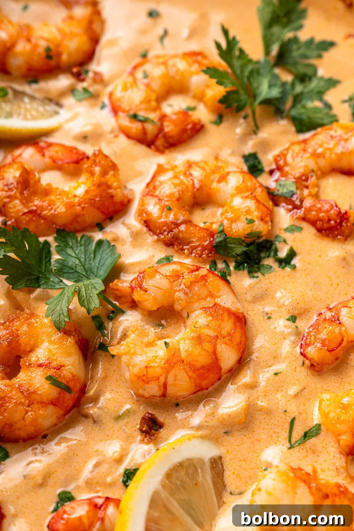 A close-up of creamy garlic butter shrimp, exquisitely garnished with fresh parsley and delicate lemon slices. The golden-brown shrimp are sumptuously coated in a rich, velvety sauce, creating an undeniably mouthwatering and visually stunning dish.