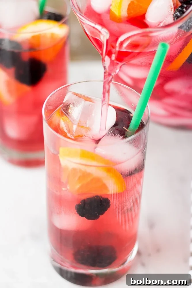 Hand holding a glass of Berry Sangria Iced Tea, showcasing its vibrant color and fresh fruit garnishes.