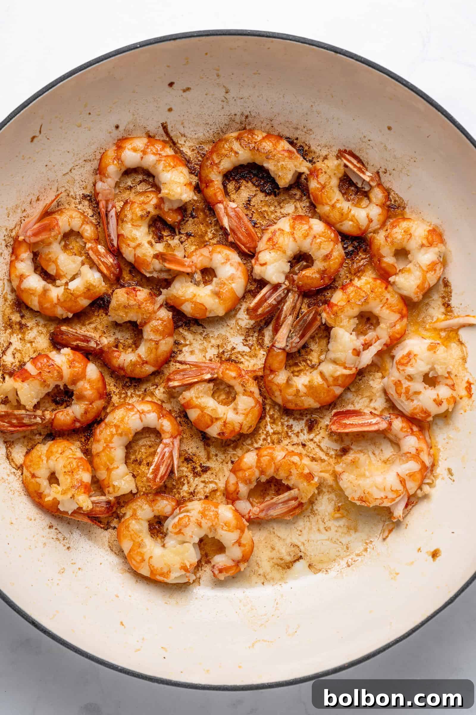 Zesty Lemon Garlic Shrimp Pasta 4 Cooked shrimp in a large white pan, seasoned and arranged in a circular pattern. The shrimp are slightly browned, indicating they were sautéed, with visible oil and spices on the pan.